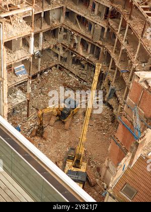 Luftaufnahme einer Baustelle mit Baggern inmitten der Trümmer eines teilweise abgerissenen Gebäudes. Stockfoto