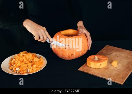 Halloween. Mädchenhände mit einem Messer schneiden orangefarbenen Kürbis, um Jacks Laterne für die Weihnachtsdekoration zu machen Stockfoto