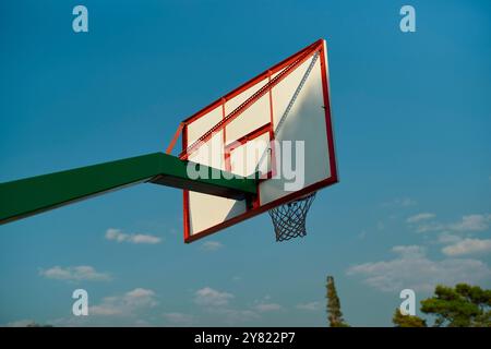 Seitenansicht eines Basketballkörpers vor einem klaren blauen Himmel mit Bäumen im Hintergrund. Stockfoto