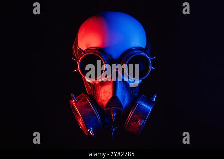 Menschlicher Schädel in Steampunk-Gläsern und einer Gasmaske mit rotem und blauem Neonlicht auf schwarzem Hintergrund Stockfoto