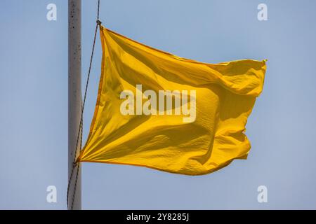 Gelbe Warnflagge auf einer Rettungsstation am Strand winkt unter blauem Himmel bei starkem Wind Stockfoto