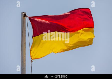 Rote und gelbe Warnflagge am Strand ist unter blauem Himmel Stockfoto