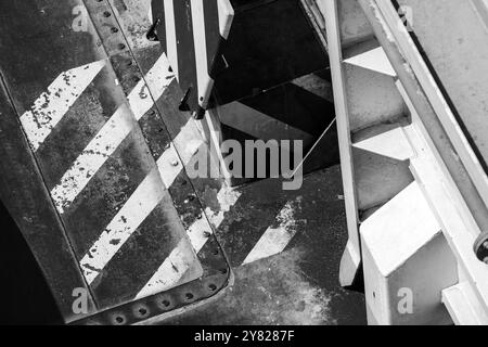 Gestreiftes Warnmuster, das über grungy Stahlplatten gemalt ist. Abstrakter industrieller Hintergrund, Schwarzweißfoto Stockfoto