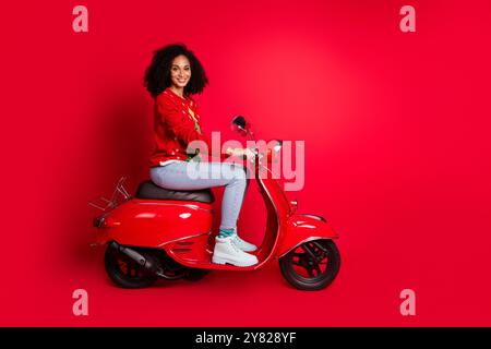 Foto von reizenden charmanten süßen Mädchen tragen roten Pullover, der Moped weihnachten Magie Wunder Zeit isoliert auf rotem Hintergrund fährt Stockfoto