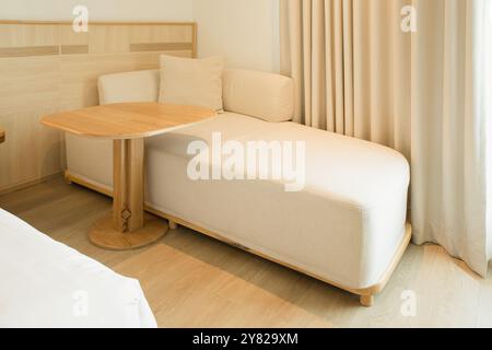 Modernes Zimmer mit minimalistischem beigefarbenem Sofa und integriertem Holztisch. Stockfoto