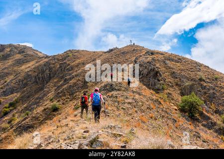 Eine Gruppe von Wanderern, die mit ihren Stangen und Rucksäcken auf einem Hügel spazieren und zum Gipfel gehen. Stockfoto