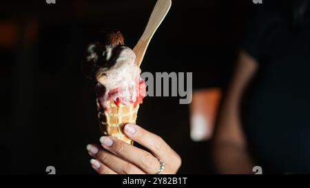 Eine Nahaufnahme einer Hand, die eine Eiskugel mit drei Kugeln verschiedener Geschmacksrichtungen hält, einschließlich Schokolade, Vanille und Erdbeere. Der Hintergrund ist Stockfoto