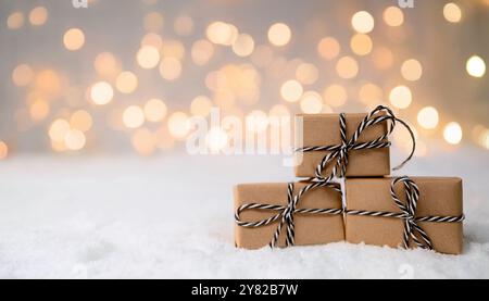 Weihnachtsgeschenke in braunem Papier gestapelt auf Schnee, gebunden mit rustikaler Schnur, minimalistische festliche Feiertagsszene, Winter Bokeh Glühlicht Hintergrund Stockfoto