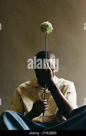 Minimales Porträt eines afroamerikanischen Mannes mit einer einzigen allium-Pflanze und einem versteckten Gesicht, das Natur, Wachstum und Schönheit symbolisiert, aufgenommen auf Film Stockfoto