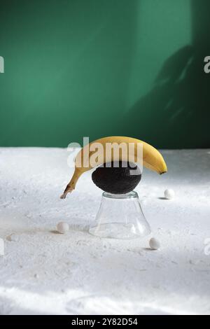 Glas mit Banane und Avocado auf weiß-grünem Hintergrund, akzentuiert von kleinen weißen Perlen, die eine frische, lebendige und stilvolle Komposition schaffen Stockfoto