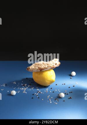 Zitronen mit Fisch-pâté-Sandwiches, ergänzt durch kleine Keramikperlen, vor blau-schwarzem Hintergrund für eine lebendige, künstlerische Komposition Stockfoto