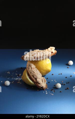 Zitronen mit Fisch-pâté-Sandwiches, ergänzt durch kleine Keramikperlen, vor blau-schwarzem Hintergrund für eine lebendige, künstlerische Komposition Stockfoto