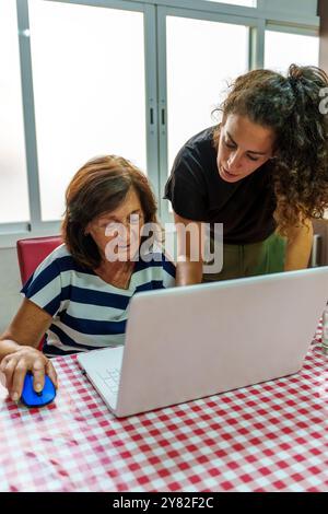 Tochter mittleren Alters lehrt älteren Müttern die Benutzung eines Laptops, um die digitale Kluft zu überbrücken Stockfoto