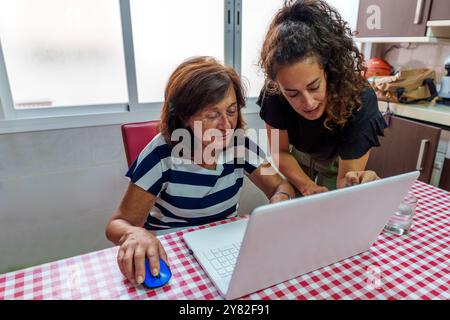 Tochter mittleren Alters lehrt älteren Müttern die Benutzung eines Laptops, um die digitale Kluft zu überbrücken Stockfoto