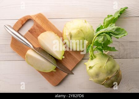 Eine ganze reife Kohlrabi und eine geschnittene liegen auf einem Holztisch mit Messer und hölzernem Küchenbrett, Makro, Blick von oben. Stockfoto