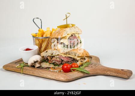 Rindersteak-Sandwich mit Rucola, Tomate und Parmesan auf einem Schneidebrett. Weißer Hintergrund. Stockfoto