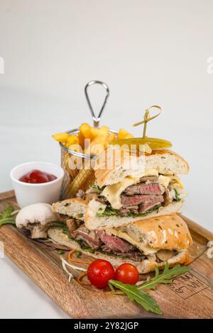 Rindersteak-Sandwich mit Rucola, Tomate und Parmesan auf einem Holzbrett. Weißer Hintergrund. Stockfoto