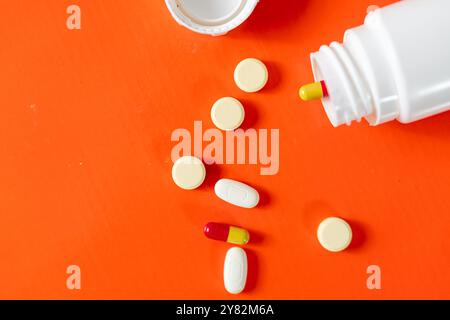 Verschiedene Pillen und Kapseln, die aus einer weißen Flasche auf orangefarbenem Hintergrund verschüttet werden. Stockfoto