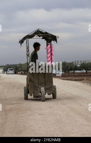 Aleppo, Syrien. 10. November 2021. Ein Straßenverkäufer, der Süßigkeitenseide verkauft, umgeben von Kindern, im Vertreibungslager Al-Zaytoun am Rande der von Rebellen kontrollierten Stadt Azaz in der nördlichen Landschaft von Aleppo. Zelte wurden in Olivenhainen entlang der türkischen Grenze errichtet, wobei die Bewohner der informellen Siedlung und ihre Kinder mit minimalen Infrastrukturen und Möglichkeiten sowie mit Platzmangel zu kämpfen haben Stockfoto