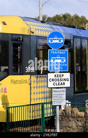 Blaue und weiße Straßenbahnwarnschilder an der Straßenbahnlinie mit dem Bienennetz, die im Hintergrund in radcliffe Greater manchester uk vorbeifährt Stockfoto