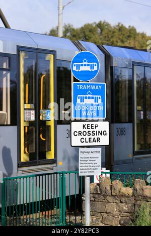 Blaue und weiße Straßenbahnwarnschilder an der Straßenbahnlinie mit dem Bienennetz, die im Hintergrund in radcliffe Greater manchester uk vorbeifährt Stockfoto