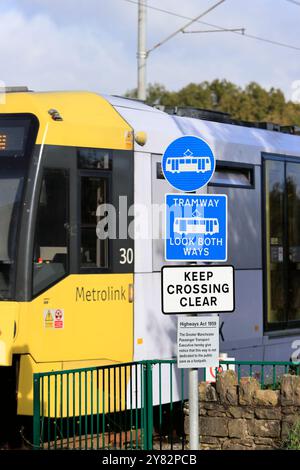 Blaue und weiße Straßenbahnwarnschilder an der Straßenbahnlinie mit dem Bienennetz, die im Hintergrund in radcliffe Greater manchester uk vorbeifährt Stockfoto