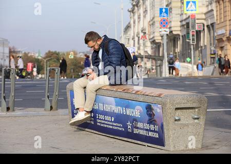 Mann, der auf der Stadtbank sitzt, mit einem Banner und einem Aufruf zum Vertragsdienst in der russischen Armee Stockfoto