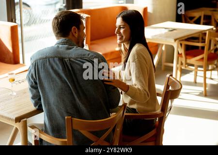 Ein Paar teilt sich einen freudigen Moment in einem Café und schlürft erfrischende Getränke, während er an einem Holztisch sitzt, umgeben von warmem Sonnenlicht und einem einladenden atmos Stockfoto