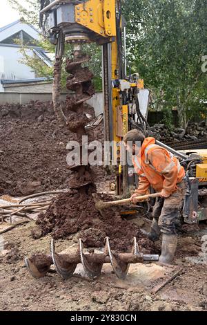 Manuelles Entfernen von Beute aus der Schneckenpfahlbohrmaschine, die Löcher in Lehmboden auf einer Hausbaustelle bohrt Stockfoto