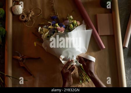 Minimaler Blick von oben auf männliche Hände binden Band auf schönen Blumenstrauß mit Bastelpapier Hintergrund Kopierraum Stockfoto