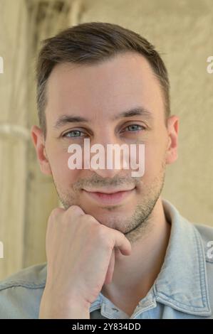 Nahaufnahme eines Mannes mit dunklen Haaren und Stoppelbart, der mit den Händen in der Nähe seines Gesichts lächelt und in die Kamera schaut Stockfoto