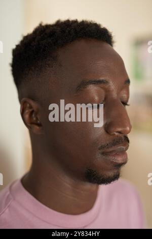 Nahaufnahme eines jungen Afrikaners, der ein T-Shirt trägt und zu Hause mit geschlossenen Augen steht Stockfoto