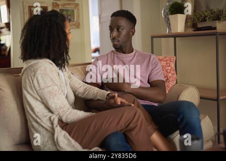 Ein junges multirassisches Paar, das ein tiefes Gespräch führt, während es zuhause auf dem Sofa sitzt Stockfoto