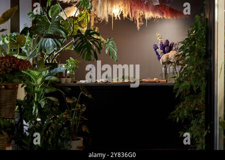 Hintergrundbild der Theke in elegantem Blumenladen mit üppigen Pflanzen in schwacher Beleuchtung, Kopierraum Stockfoto