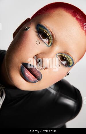 Eine junge Frau mit kurzen rosa Haaren zeigt ihren gewagten Stil und ihr eklektisches Make-up in einer lebendigen Studioatmosphäre. Stockfoto