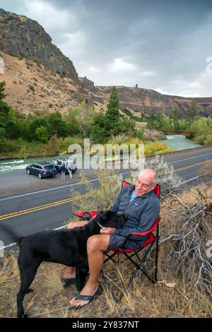 Ein Mann mit einem Senior entspannt sich mit seinem schwarzen Labor entlang des Highway 12 im Tieton River Canyon außerhalb von Yakima, Washington Stockfoto