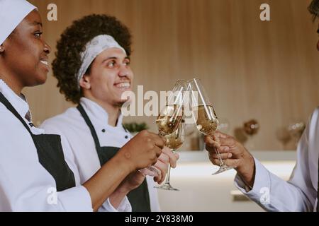 Niedrigwinkelaufnahme von afroamerikanischen Köchinnen und männlichen Sous-Köchen und Koch, die Gläser anschlagen Stockfoto