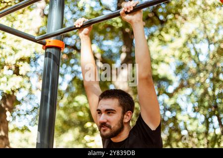 Sportmann dehnt sich im Herbst im Park aus und macht Übungen. Gutaussehender Mann macht Dehnungsübungen im Herbstpark. Sonnenuntergang im Park mit Bäumen und grünem Gras Stockfoto