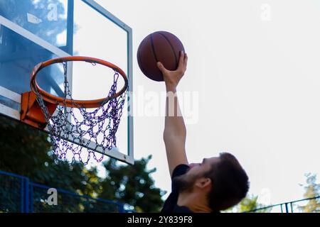 Gutaussehender Basketballspieler, der einen Ball durch den Basketballkorb schießt, während er draußen auf dem Basketballfeld spielt Stockfoto