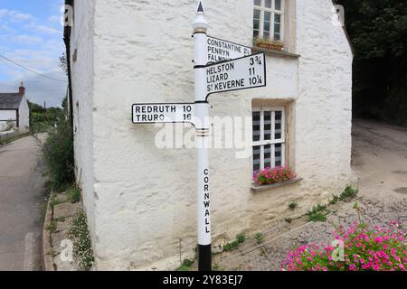 Ein altmodisches gusseisernes Schild führt Reisende zu berühmten Städten und Dörfern in Cornwall, mit der Kulisse eines typischen kornischen Ferienhauses Stockfoto