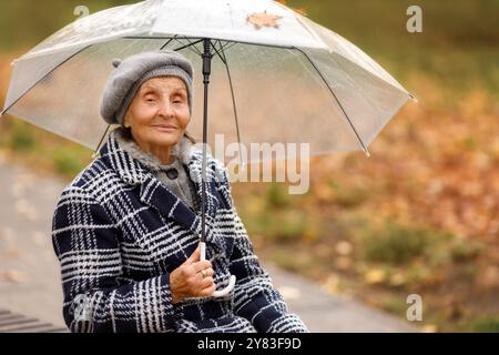 Ältere Frau im grauen Mantel mit Regenschirm im Herbst Stockfoto