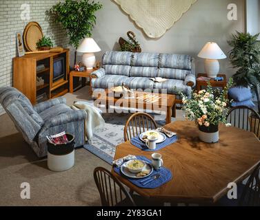 Gemütliches Vintage-Wohnzimmer und Essbereich mit blauen Polstermöbeln, Holztischen, Lampen, Pflanzen und klassischer Inneneinrichtung in warmen Farben. Stockfoto