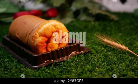 Ein goldbraunes Brot, das weich aussieht, wird in einen braunen Plastikbehälter gelegt, der auf grünem Kunstrasen liegt und mit Laub und roten Blumen geschmückt ist Stockfoto