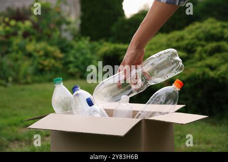 Recyclingkonzept. Mann, der Plastikflasche draußen in Pappkarton steckt, Nahaufnahme Stockfoto