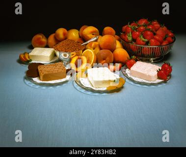 Verschiedene Frischkäsesorten mit Fruchtgeschmack, frische Erdbeeren, Aprikosen, Orangen mit Kuchen, Butter und braunem Zucker auf dem Tisch, buntes Stillleben Stockfoto