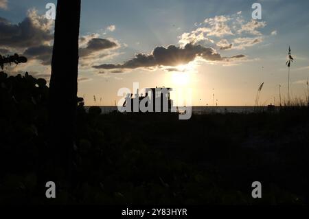 Silhouette am St. Pete Beach, FL in Richtung Golf von Mexiko, da schwere Maschinen auf der Strandernährung arbeiten. Blick auf Sand und Hafer. Nahe Sonnenuntergang spät Stockfoto