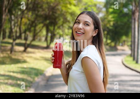 Brasilianische junge Frau trinkt roten Entgiftungssaft mit Rote-Bete-Orangen-Karotte draußen Stockfoto