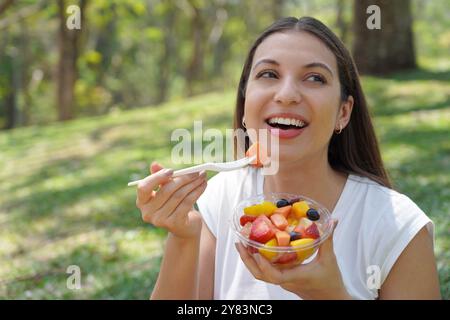 Nahaufnahme einer jungen Frau, die einen Obstsalat im Park isst. Sieht seitlich aus. Stockfoto