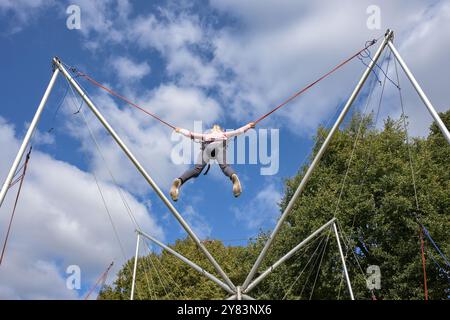 Das kleine Kind von hinten hat Spaß beim Springen auf einem Bungee-Trampolin hoch in den Himmel, Freizeit Outdoor-Aktivitäten auf einem Festival, Kopierraum und ausgewählte Schwerpunkte Stockfoto