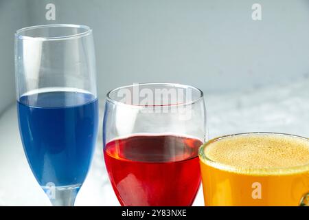 Drei flüssige Gläser in Rot, Blau, Gelb, Bargetränke für Party, Regenbogenbier in Gläsern Stockfoto